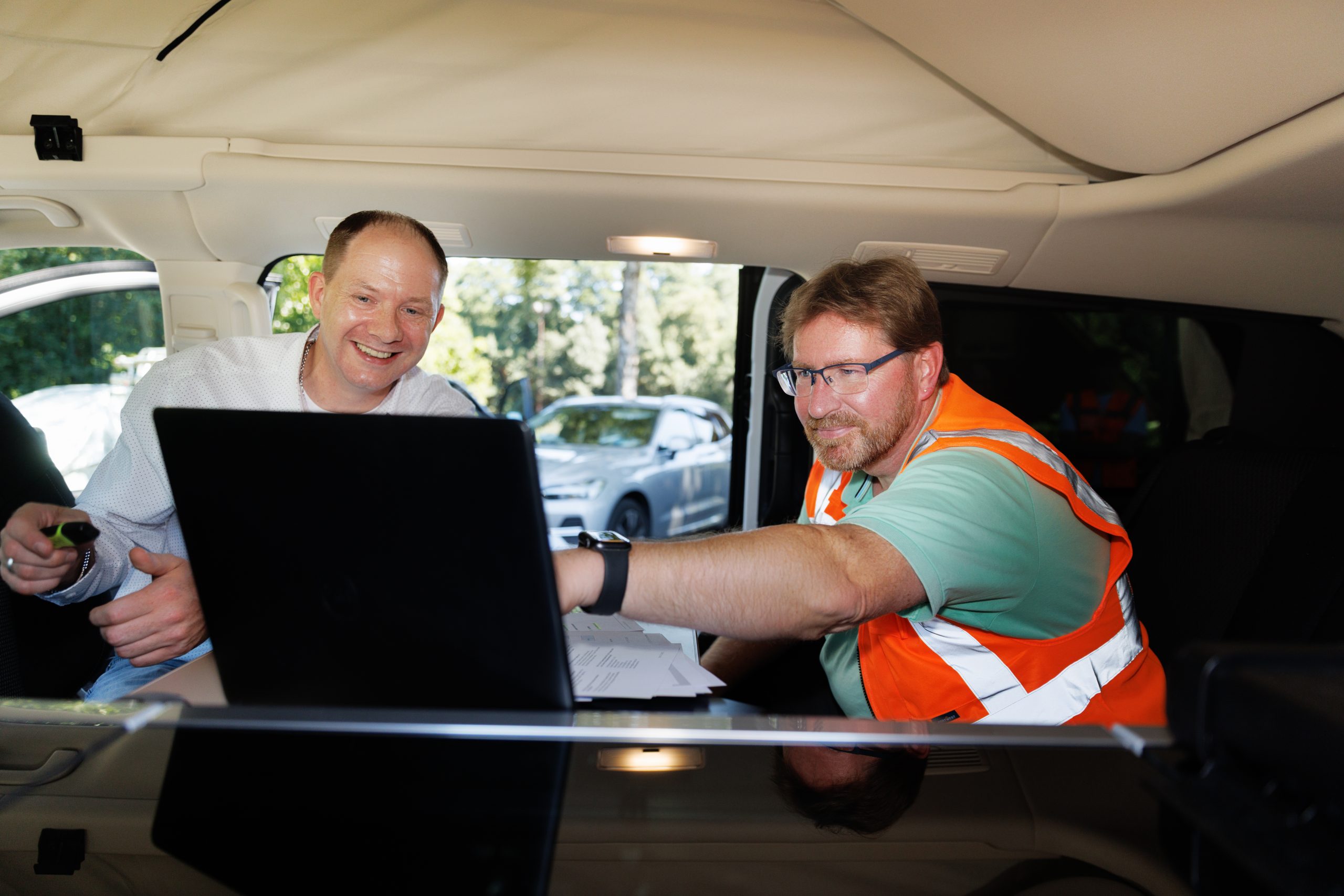Mitarbeiter aus Bau und Handwerk besprechen digitale Vorsorge- und Versicherungslösungen mit Laptop im Servicefahrzeug